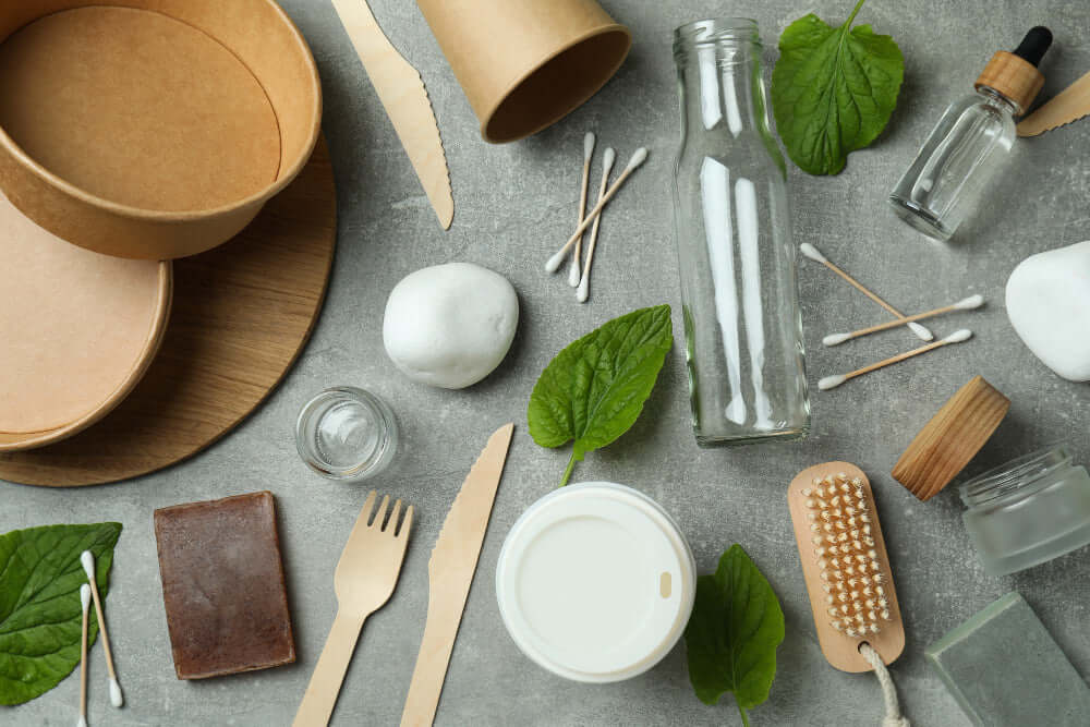 A flat lay of natural products and eco-friendly packaging, including jars, bamboo utensils, and green leaves.