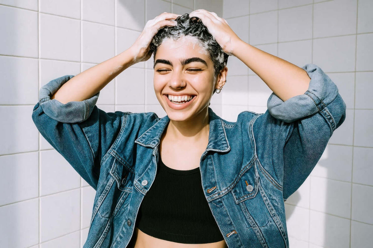 Smiling young woman washing her hair in the shower, showcasing a joyful hair care routine.