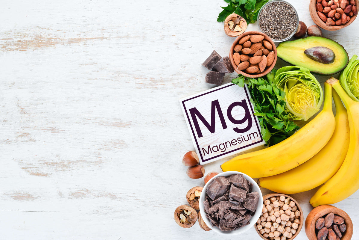 Assorted magnesium-rich foods including bananas, nuts, and leafy greens on a wooden surface.