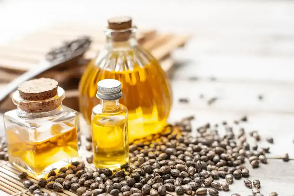 Assorted glass bottles of castor oil surrounded by castor seeds on a bamboo mat.