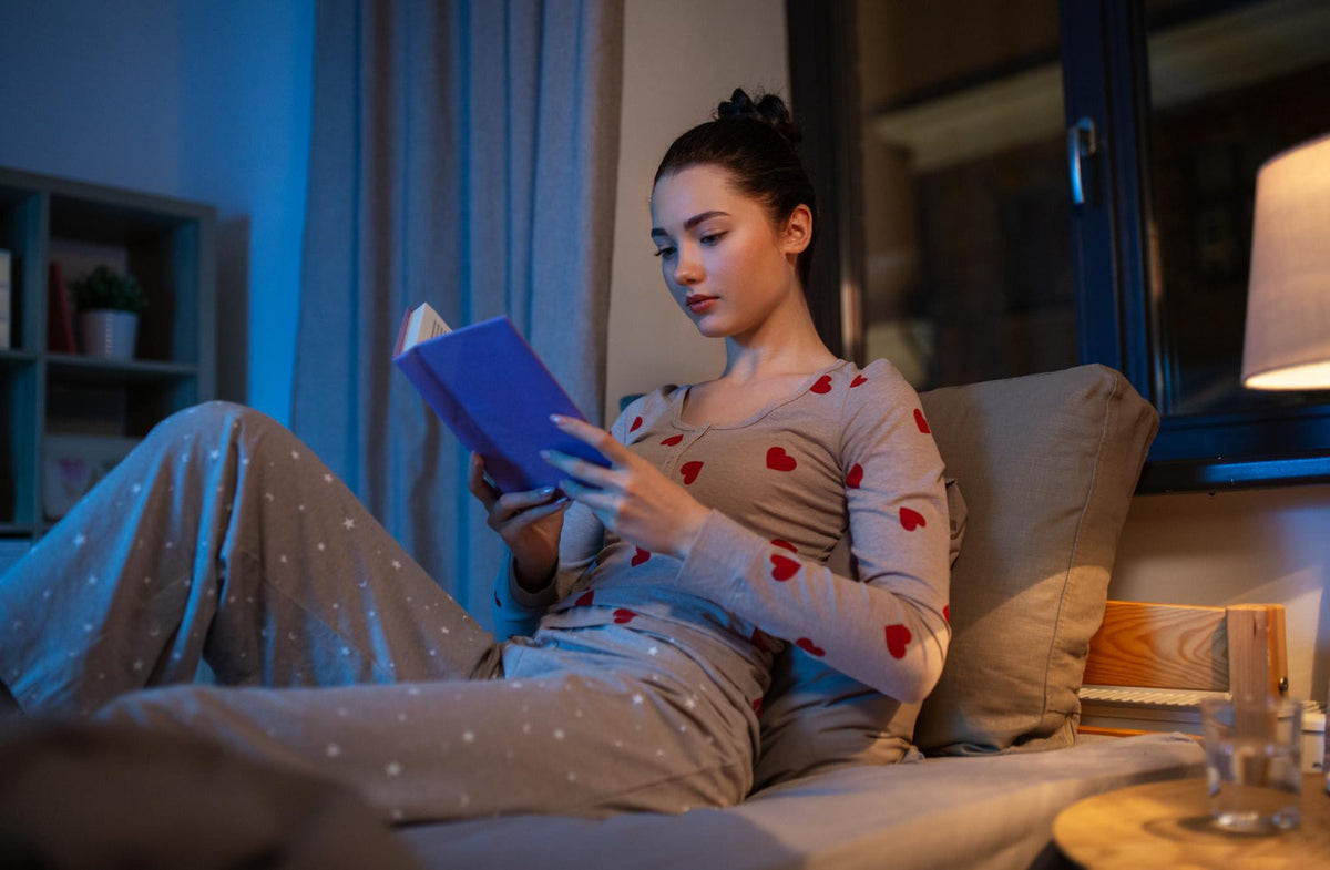 Woman winding down in warm bedroom light with a glass of water and a simple bedtime trial checklist.